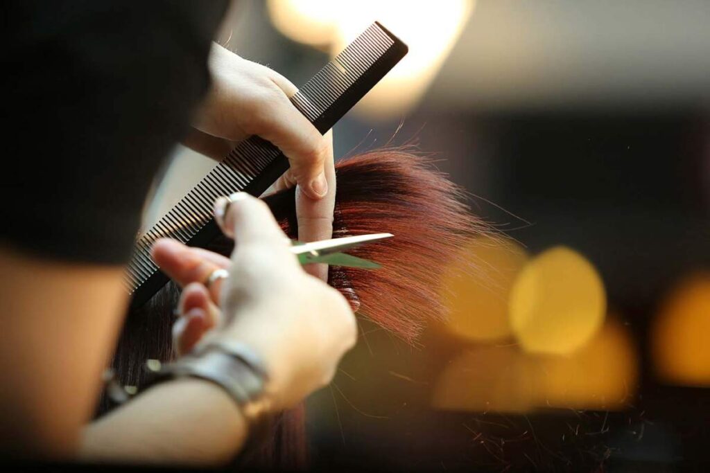 A person detangling long, wet hair gently with a wide-tooth comb near a bathroom sink.